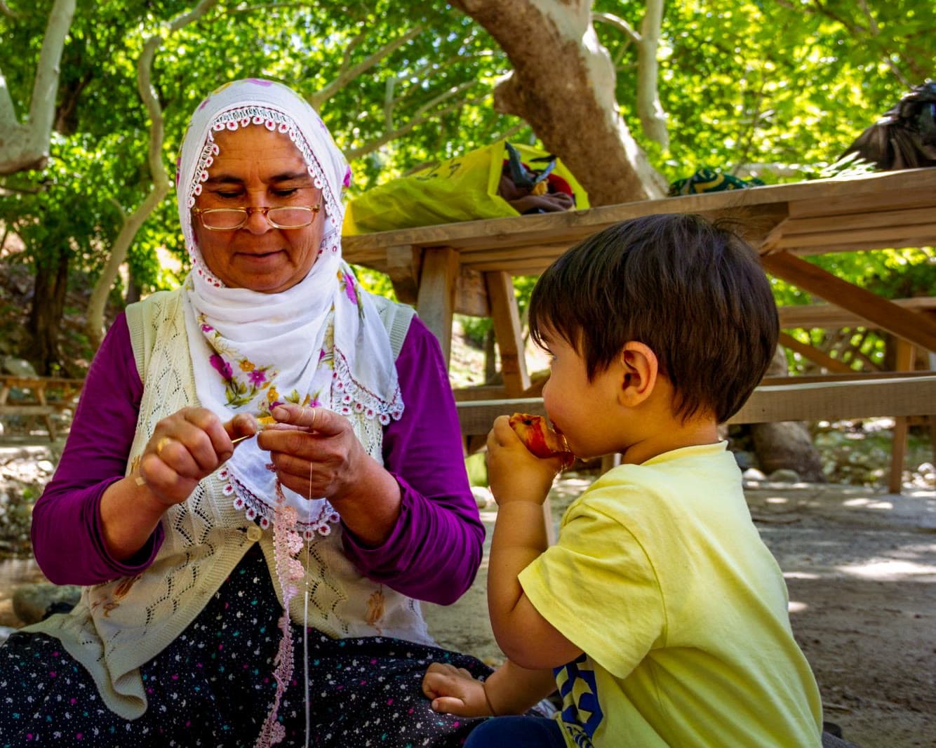 A young child watches an adult crochet lace with a hook and yarn.