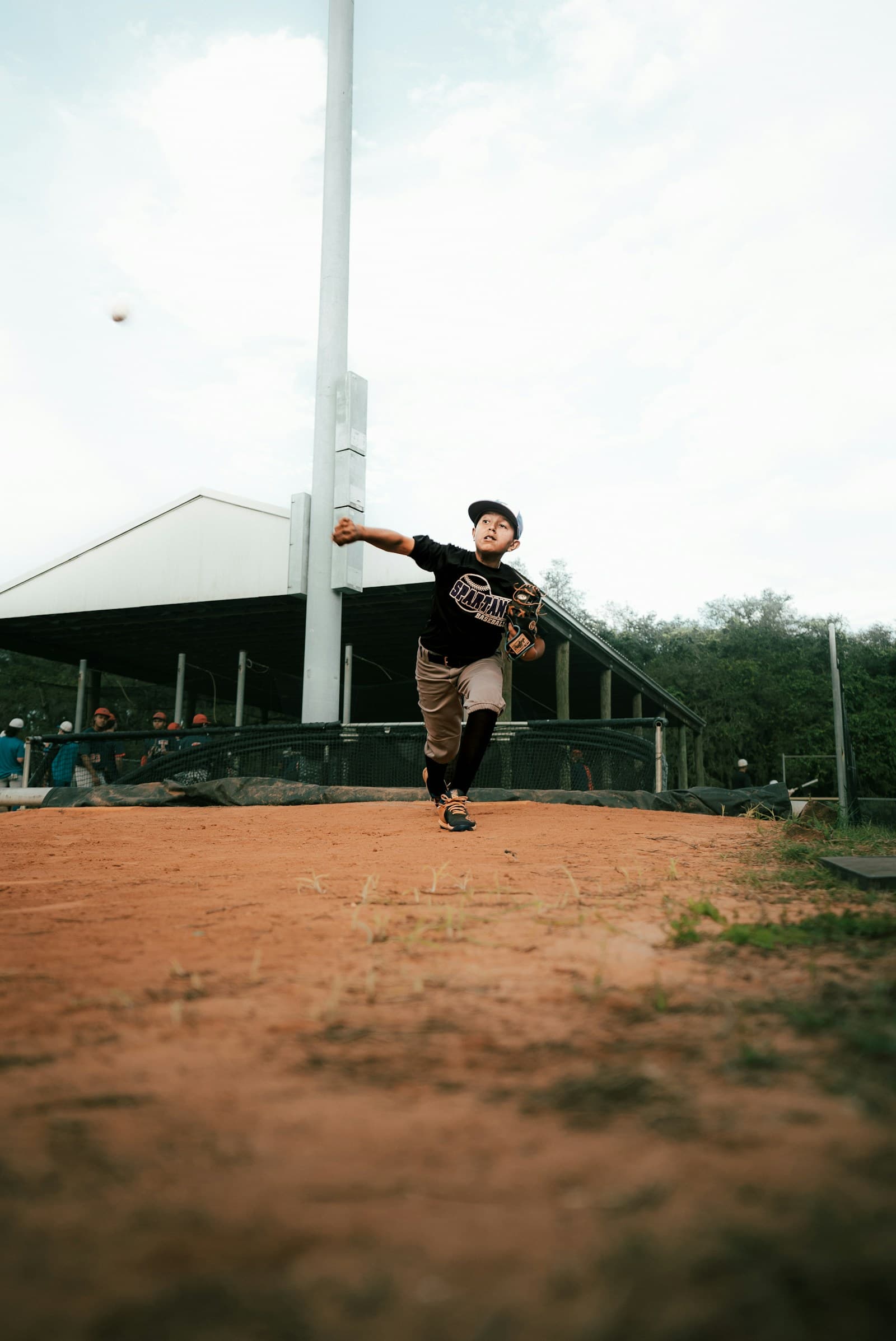 A young baseball player pitching on a dusty community field.