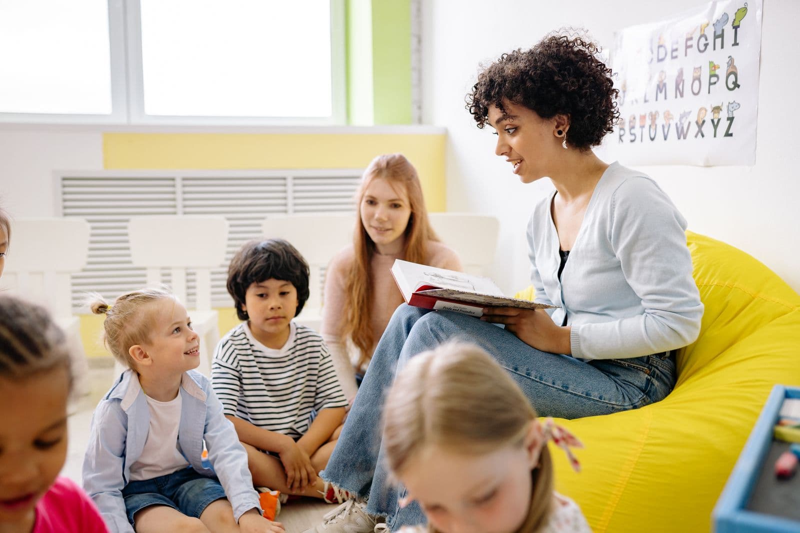 A teacher smiling while reading with a small group of engaged students.
